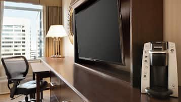 A hotel room with a desk, a flat-screen TV, a coffee maker, and a chair.