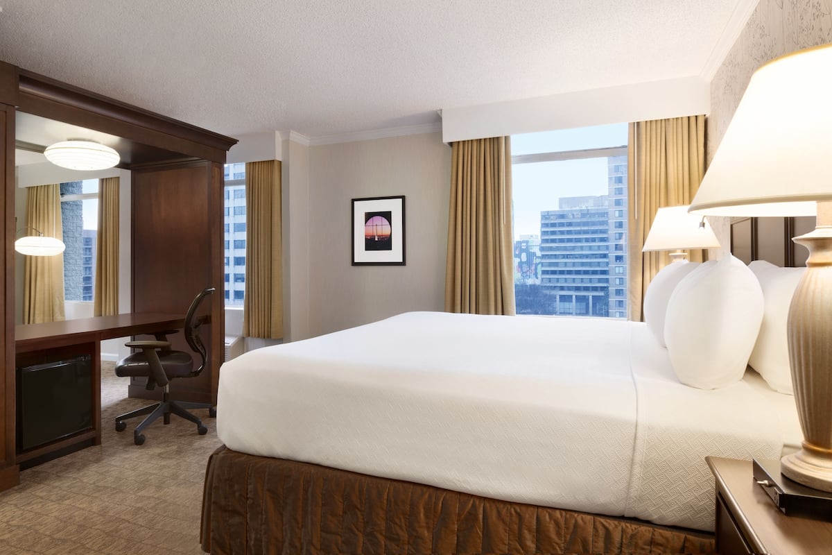 A hotel room with a large bed, a desk, a chair, and a window with curtains.