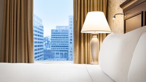 Une chambre d’hôtel avec un lit, une lampe et une vue sur les bâtiments de la ville, visible par la fenêtre.
