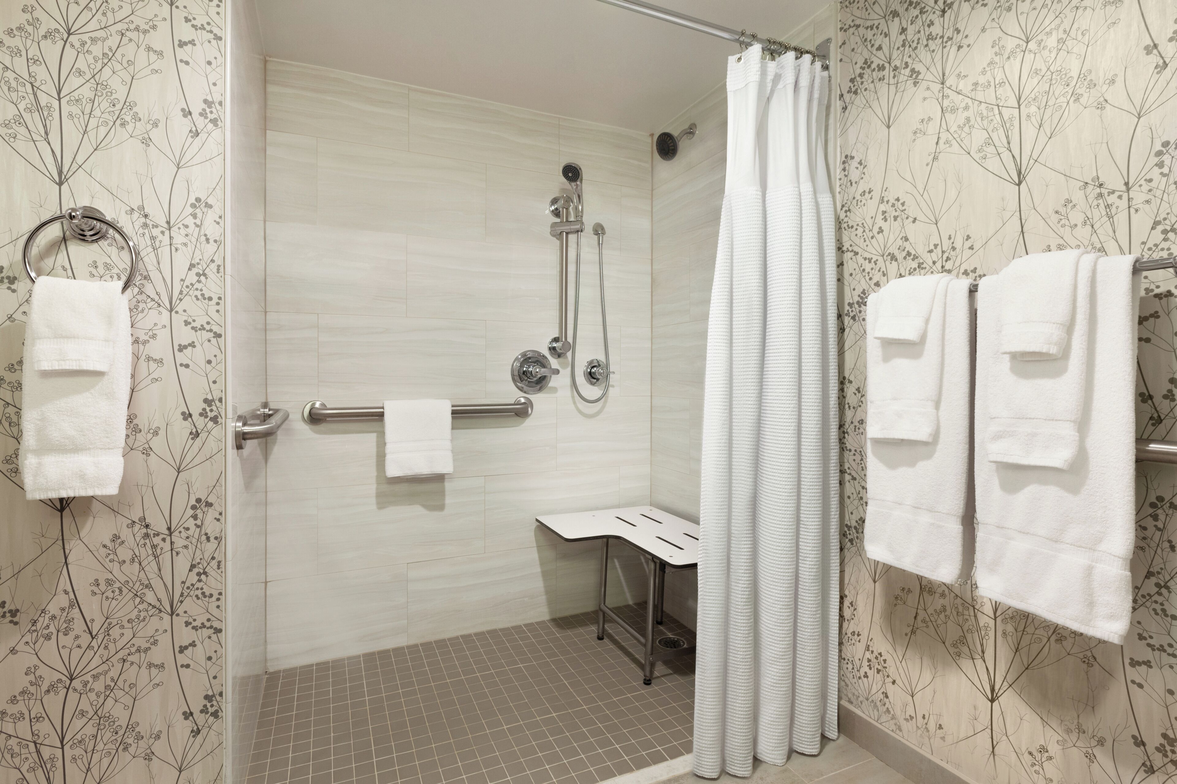 A shower area with a glass door, a handheld showerhead, a towel rack, and a bench.