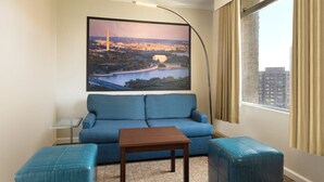 Une chambre d’hôtel avec un canapé bleu, une table basse en bois et une grande fenêtre avec des rideaux.