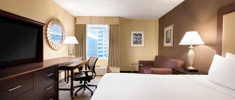 A hotel room with a bed, a desk with a chair, a television, a lamp, and a window with curtains.