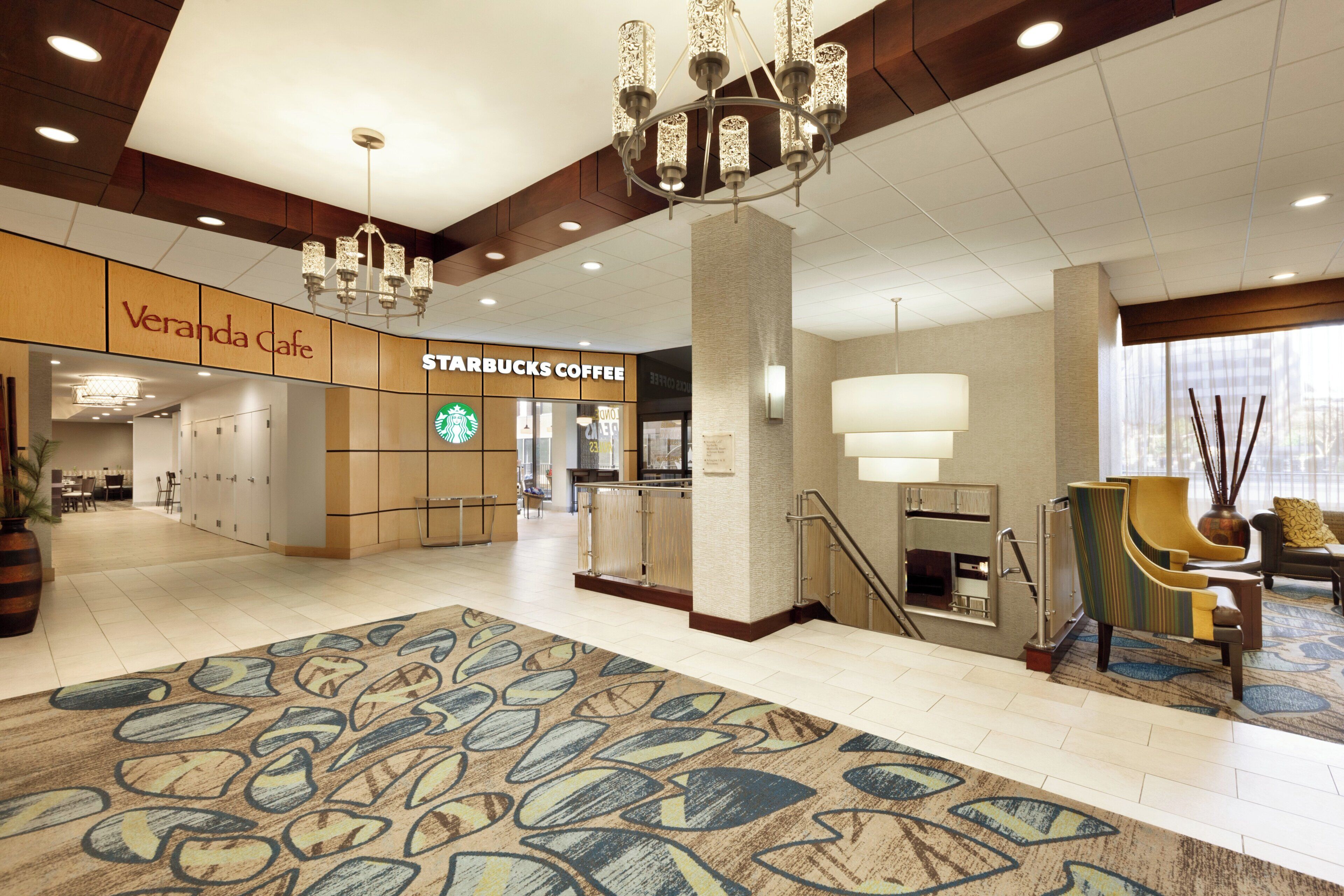A spacious lobby with a Starbucks Coffee, Veranda Cafe, and a chandelier.