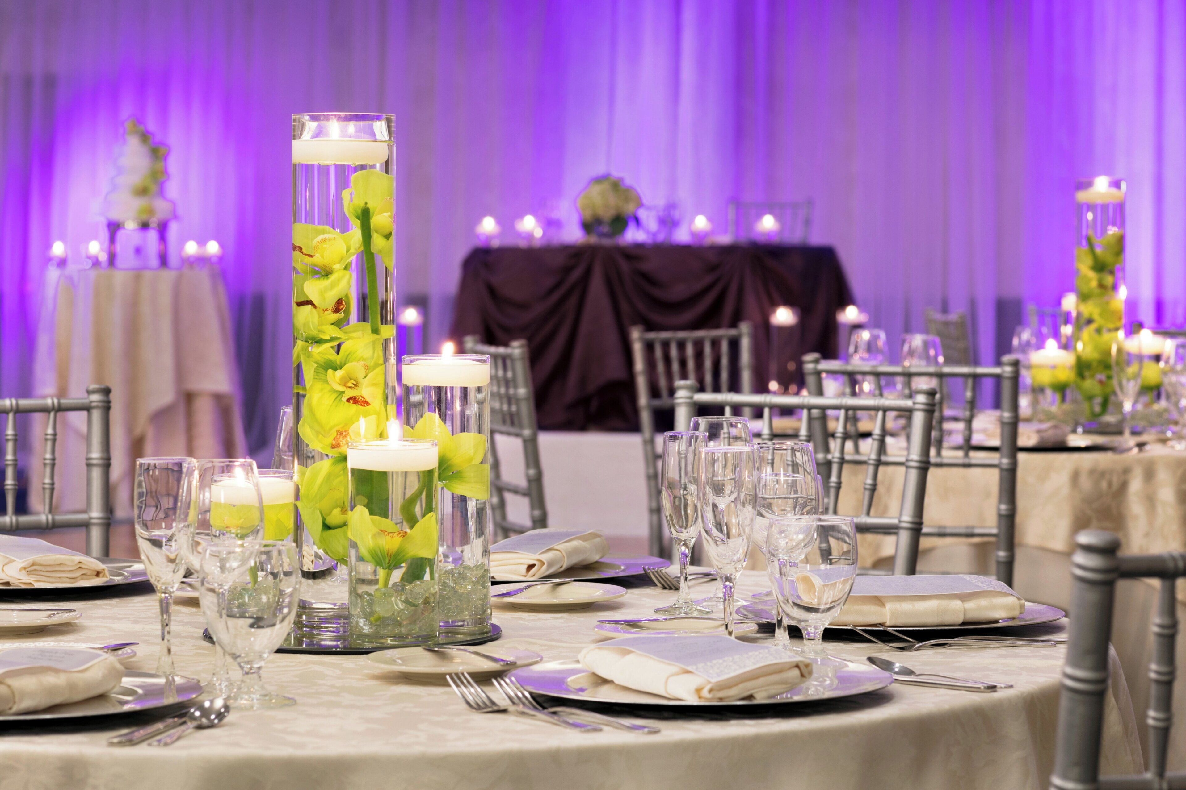 Una mesa dispuesta para un evento formal, con cristalería transparente, servilletas dobladas y candelabros.