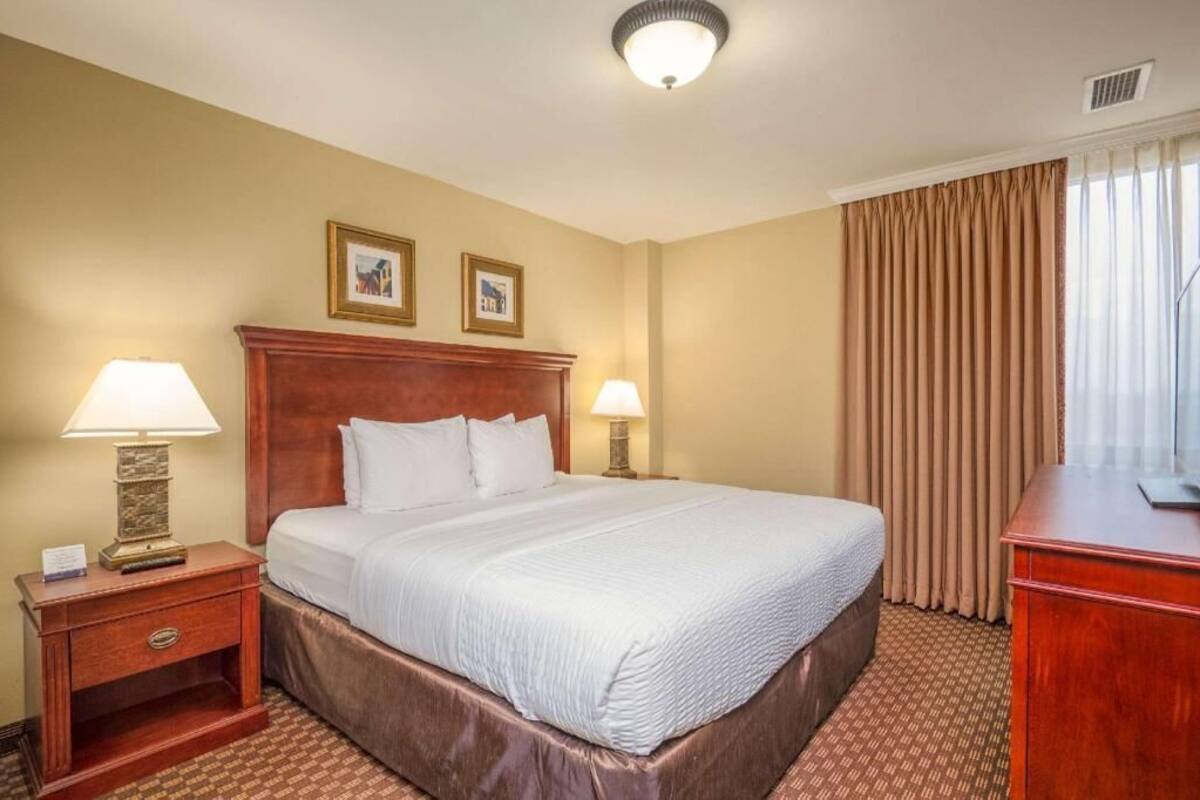A hotel room with a large bed, two bedside lamps, a wooden headboard, a desk, and two framed pictures on the wall.