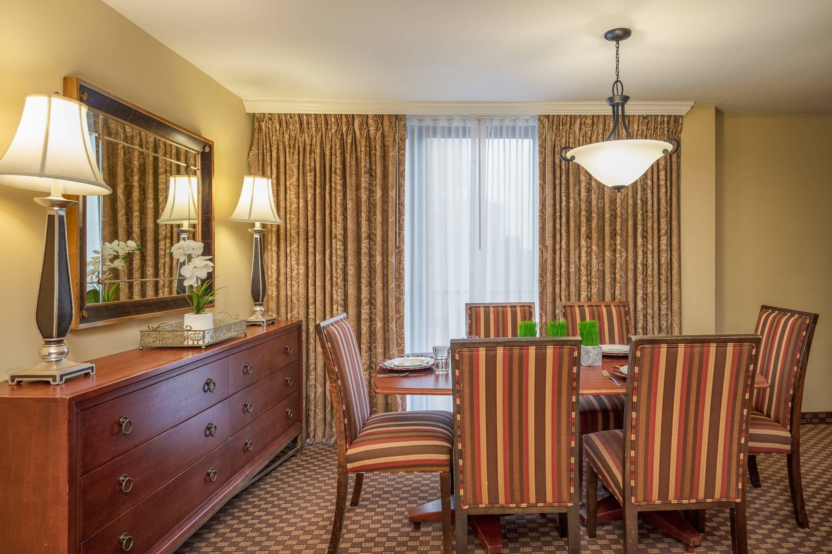 A hotel dining area with a wooden buffet, striped chairs, a chandelier, and a large mirror.
