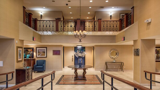 A hotel lobby with a grand staircase, a chandelier, and a round table with a vase of flowers. - Arlington Court Suites, a Clarion Collection Hotel (Arlington)
