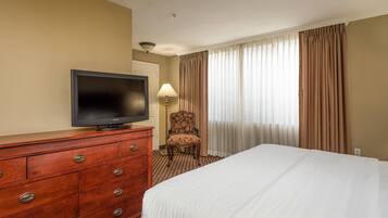 A hotel room with a bed, a TV on a wooden dresser, a chair, and a window with curtains.