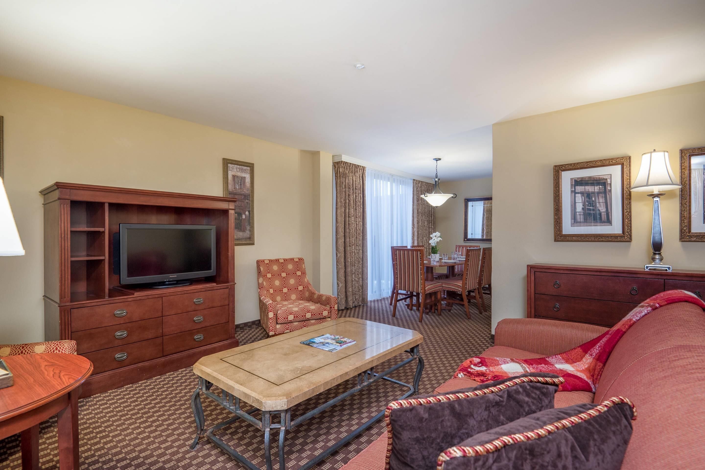 A hotel room with a television, a sofa, a dining table, and a chair.