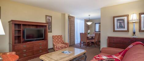 A hotel room with a television, a sofa, a dining table, and a chair.