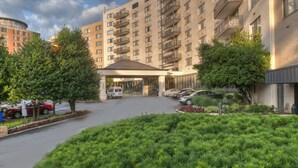 A multi-story hotel with a curved facade, a covered entrance, and a parking area with cars. - Arlington Court Suites, a Clarion Collection Hotel (Arlington)