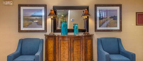 A lobby with two blue armchairs, a wooden console table with decorative items, framed landscape paintings, and a mirror above the console.