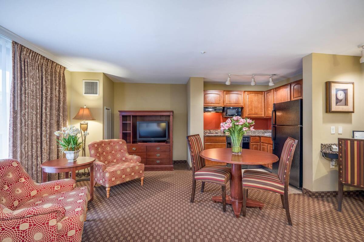 A hotel room with a dining area, a TV, and a kitchen.
