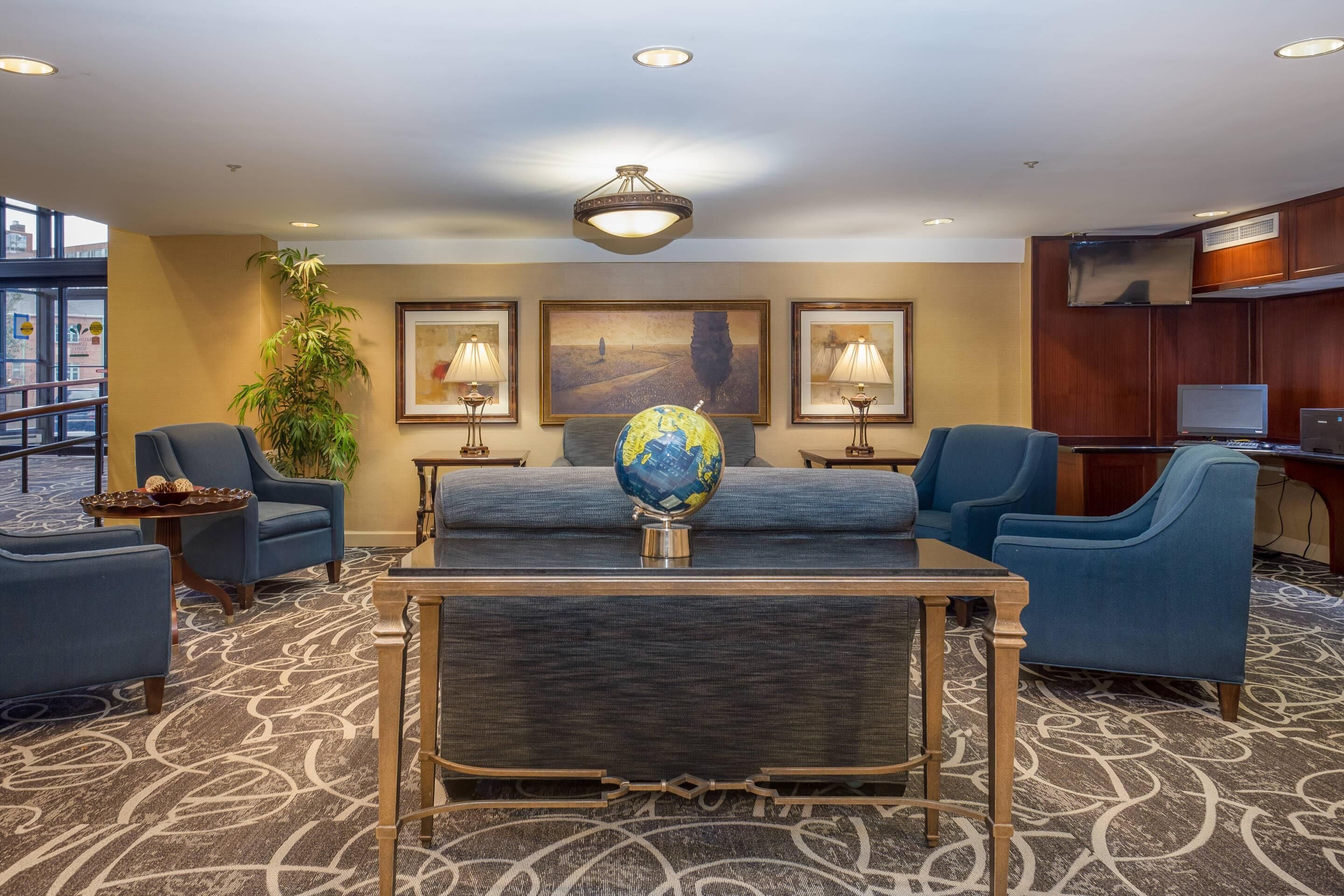 A lobby with a sofa, chairs, a globe, framed artwork, and a TV.