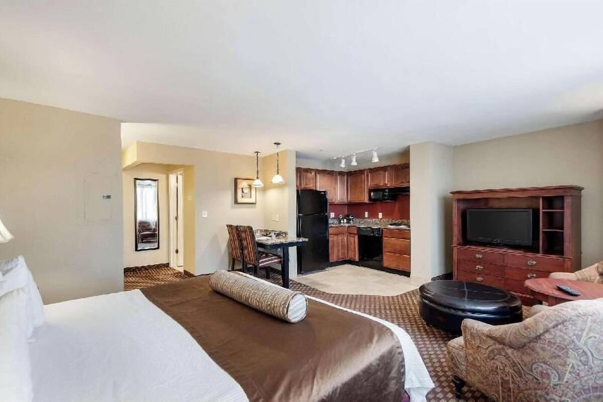 A hotel room with a bed, a small dining table, a kitchen area, and a TV.