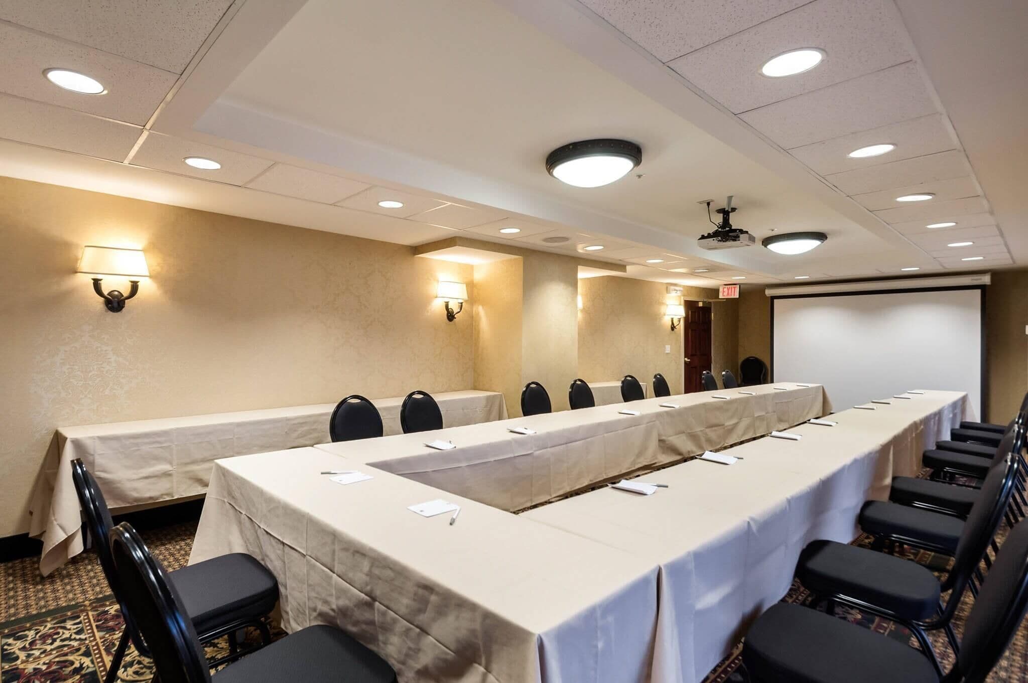 A conference room with a long table, chairs, and a projector screen.