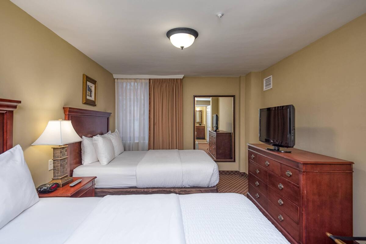 A hotel room with two beds, a TV, a dresser, a lamp, and a mirror.