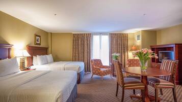 A hotel room with two beds, a dining table with chairs, a TV, and a window with curtains.