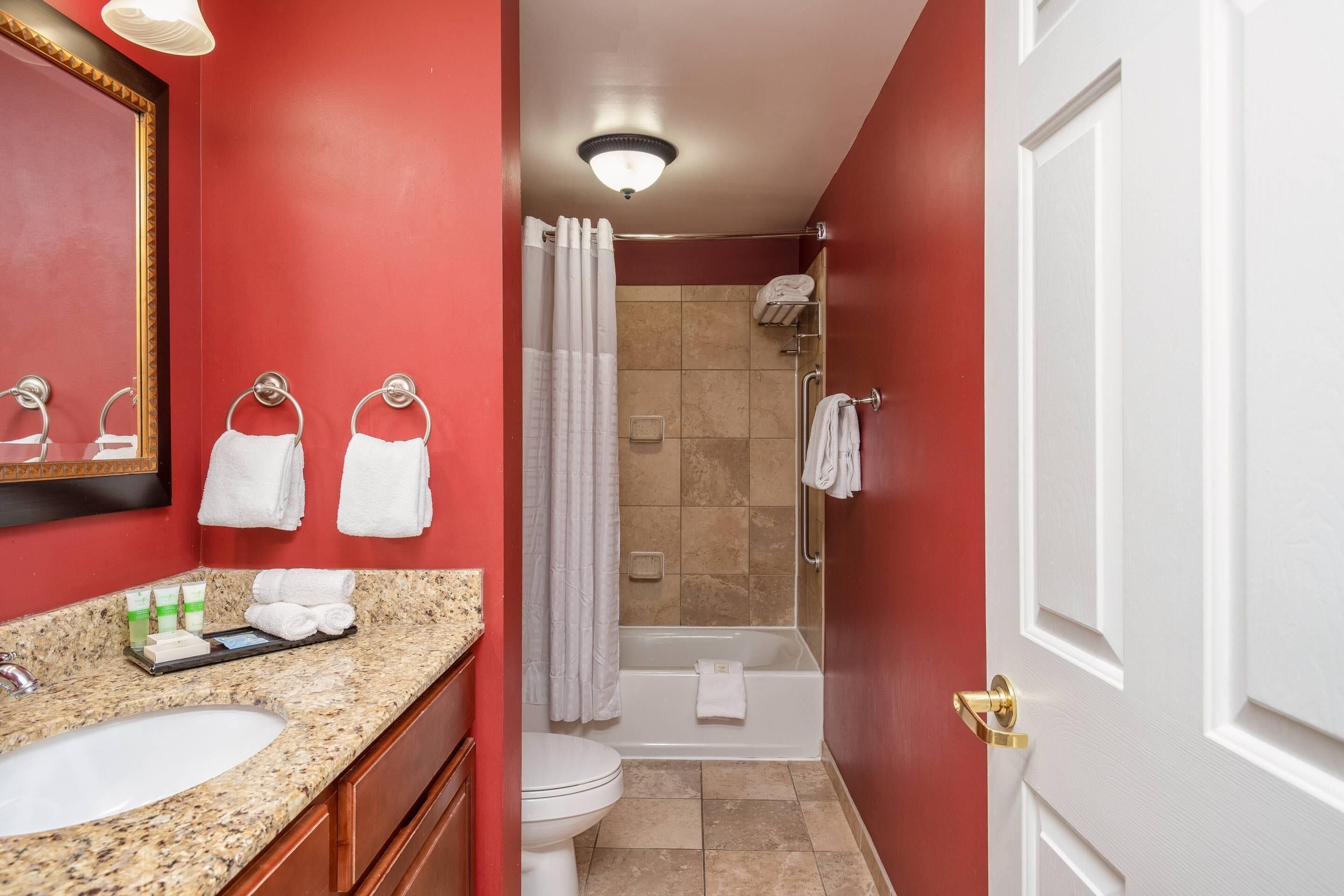 Une salle de bain dotée d’un comptoir en granit, d’un lavabo, de toilettes, d’une douche avec une porte en verre et d’une baignoire.