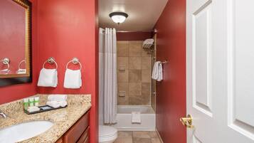 Une salle de bain dotée d’un comptoir en granit, d’un lavabo, de toilettes, d’une douche avec une porte en verre et d’une baignoire.