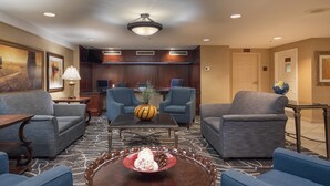 A hotel lobby with a seating area, a coffee table with a dessert, and a kitchen in the background. - Arlington Court Suites, a Clarion Collection Hotel (Arlington)