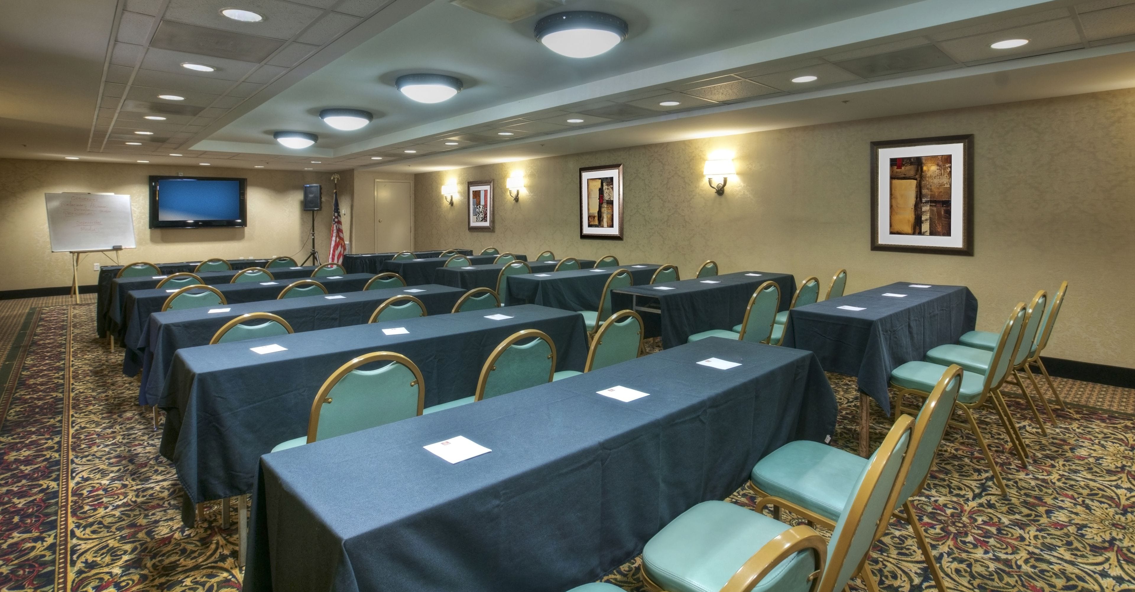 Une salle de conférence avec des rangées de tables et de chaises, un tableau blanc, un téléviseur et des œuvres d’art encadrées accrochées aux murs.