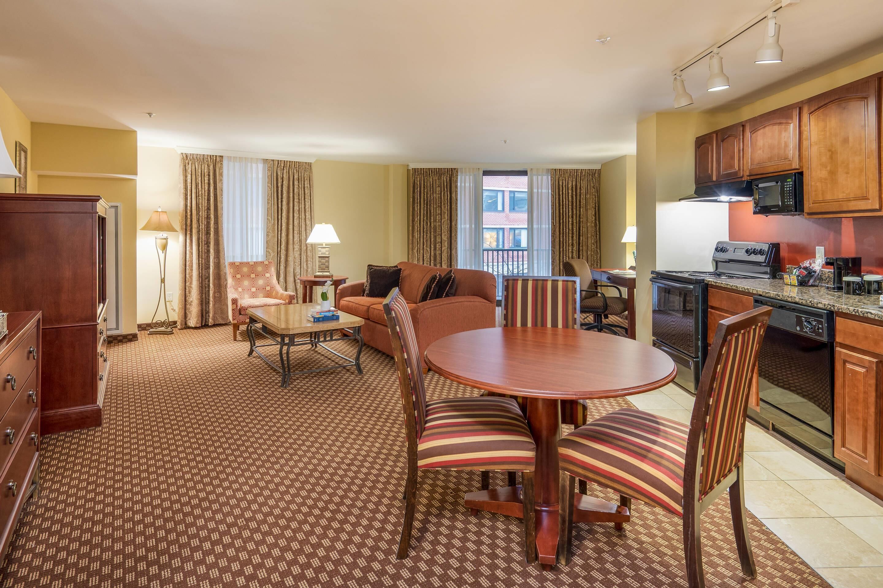Een hotelkamer met een zithoek, een eettafel, een keuken en een groot raam met gordijnen.