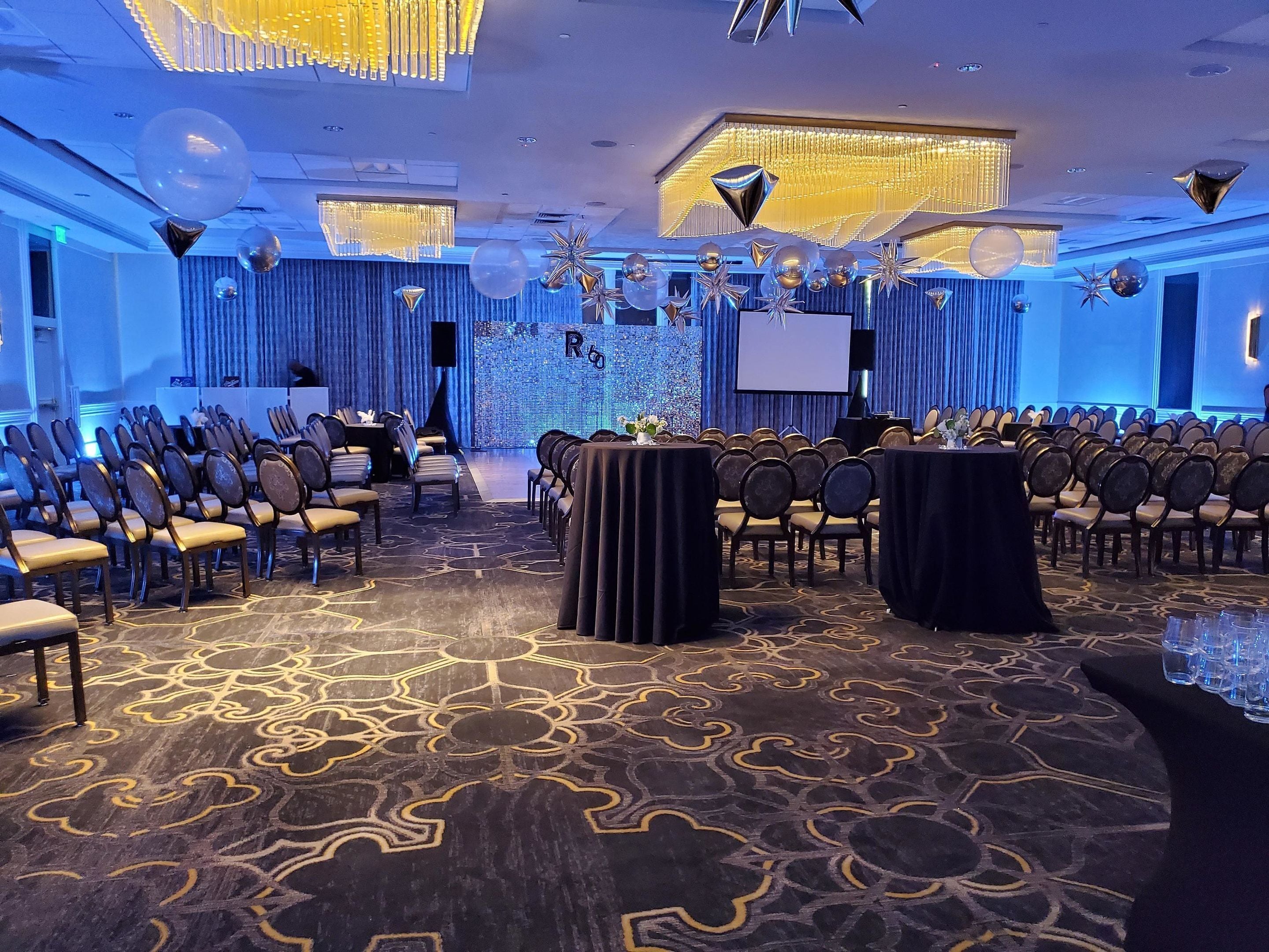 A conference room with rows of chairs, a stage with a screen, and a patterned carpet.