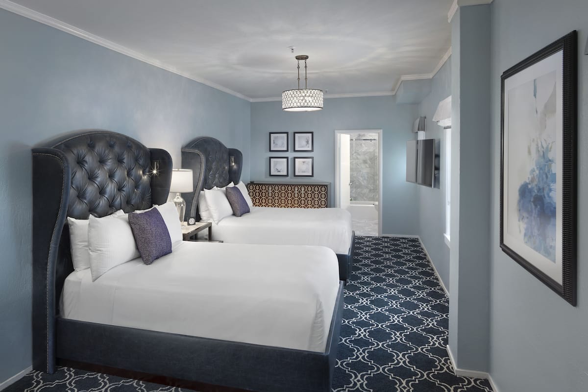 Ett hotellrum med två sängar, en kristallkrona, inramade konstverk och en mönstrad matta.