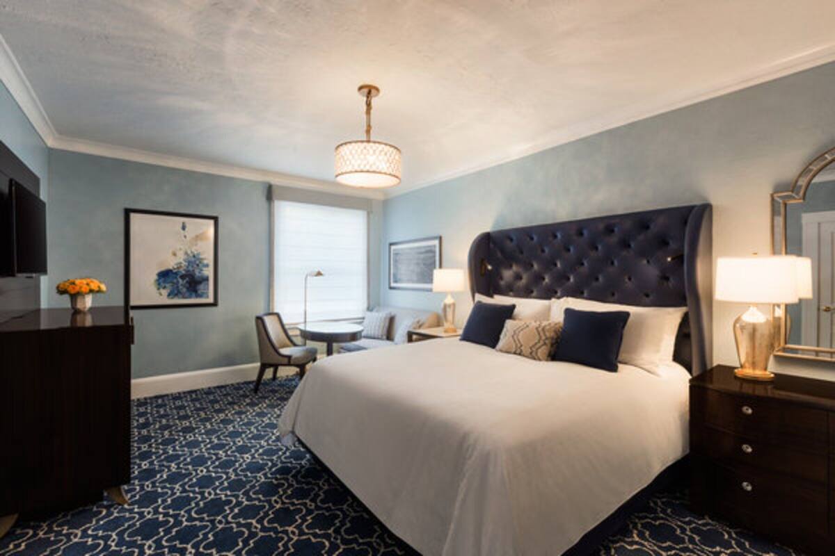 Ett hotellrum med en stor säng, ett skrivbord, en stol, en tv och en lampa.