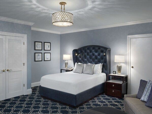 A bedroom with a large bed, two bedside tables, a chandelier, and a patterned carpet.