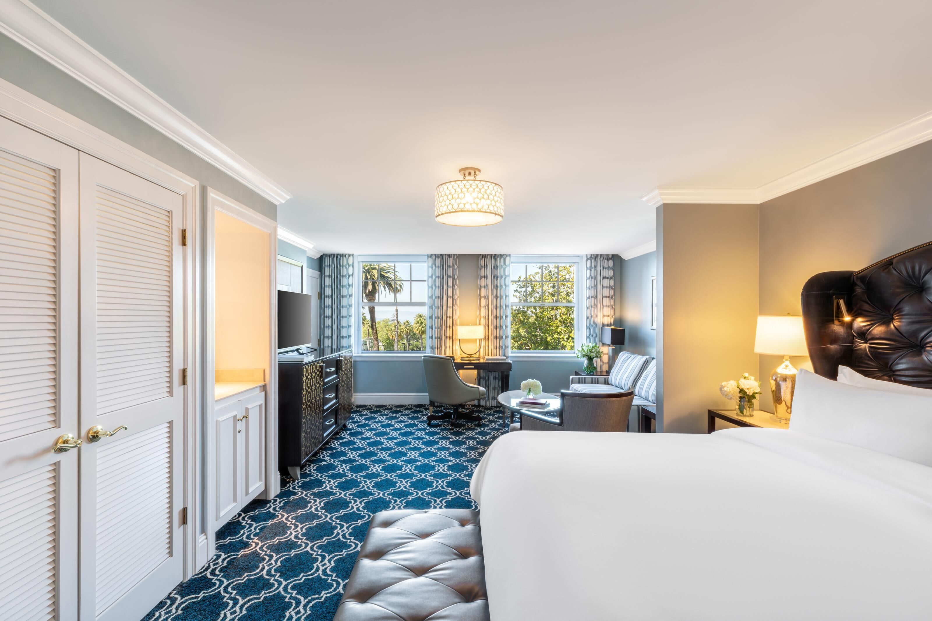 Habitación de hotel con cama, escritorio, silla, lámpara y vistas al exterior.