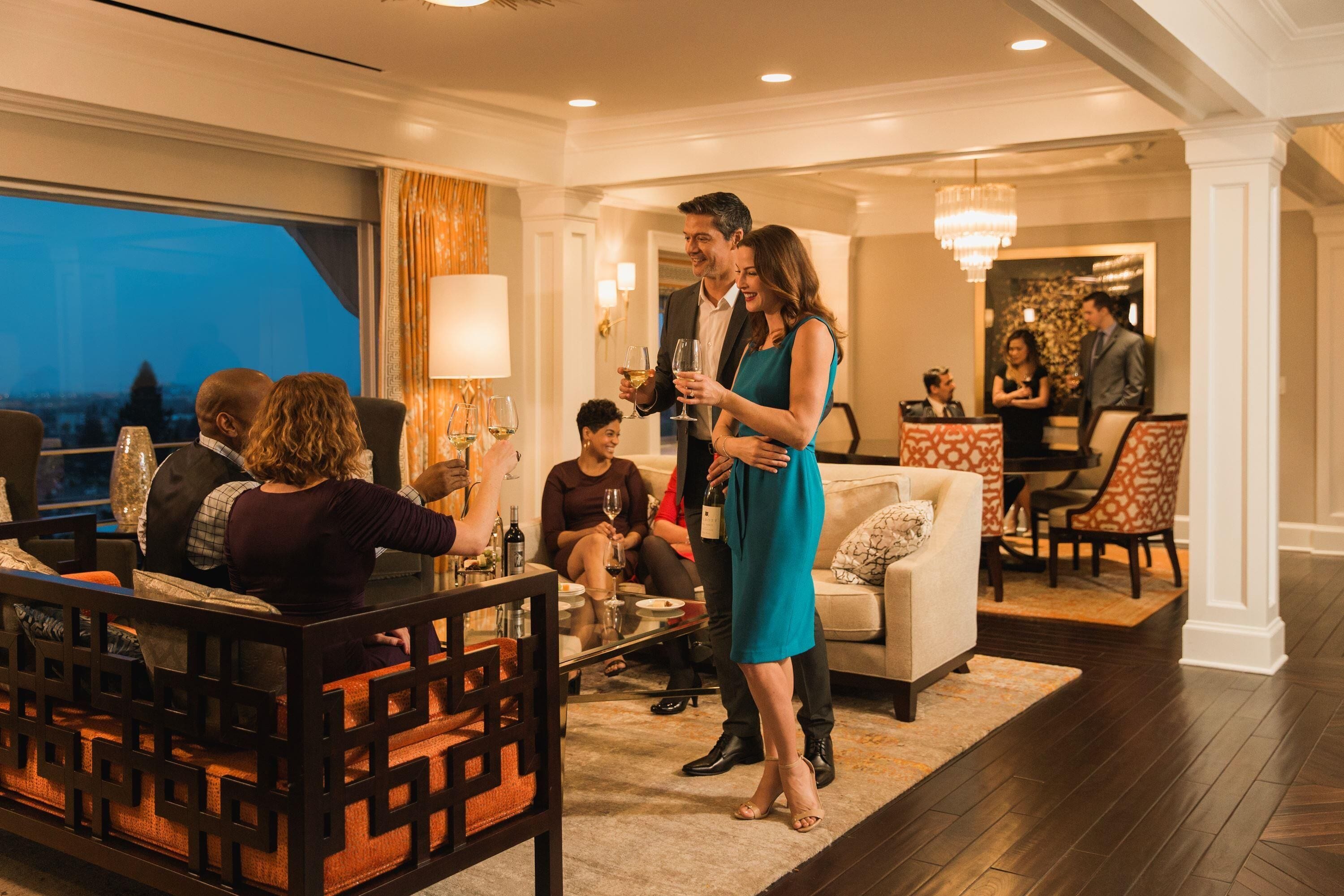 A modern hotel lobby with a seating area, a dining space, and a view of the city at night.