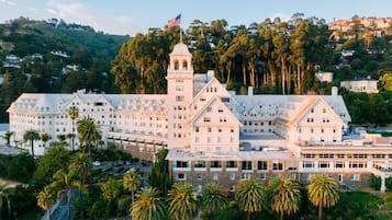 A large, multi-story hotel with a prominent tower, surrounded by palm trees and set against a hilly backdrop.