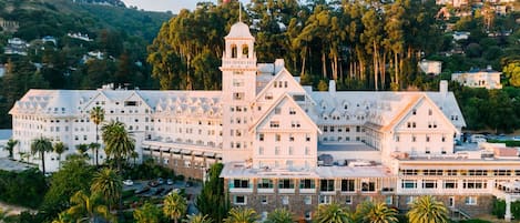 A large, multi-story hotel with a prominent tower, surrounded by palm trees and set against a hilly backdrop.
