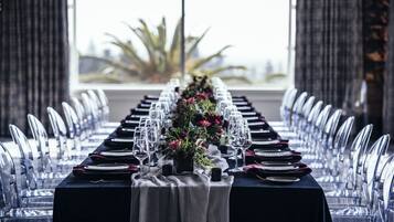 Et langt spisebord med transparente stole, dækket med tallerkener, glas og en midterdekoration.