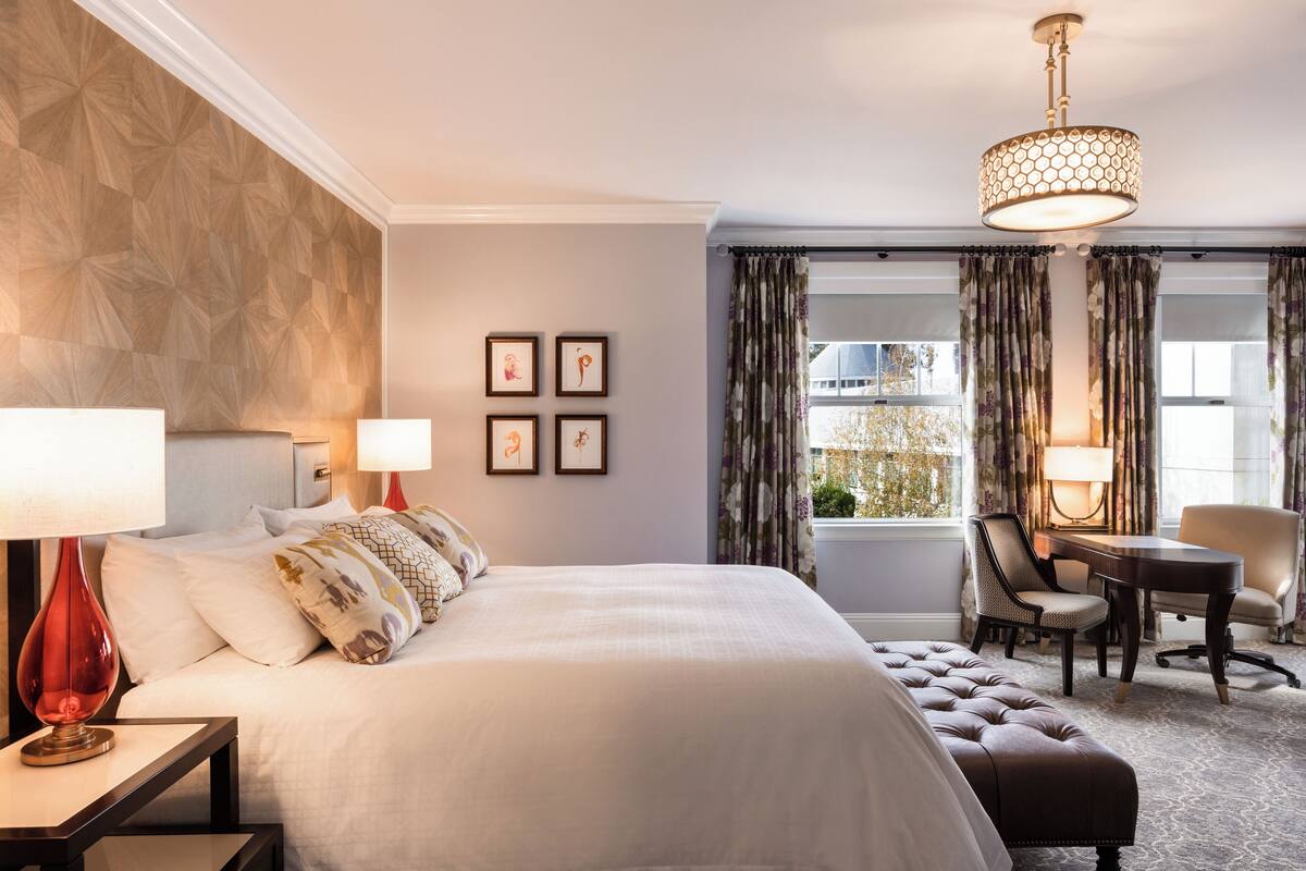 Ett hotellrum med en stor säng, ett skrivbord och en stol. Det finns fyra inramade tavlor på väggen.