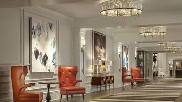 A spacious hotel lobby with modern chandeliers, leather armchairs, and large abstract paintings on the walls.