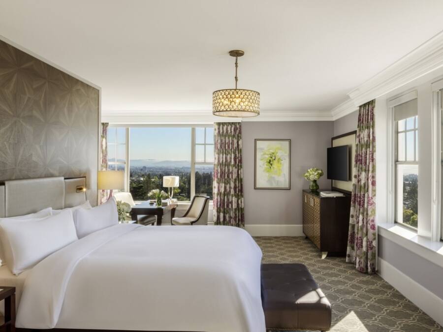 A hotel room with a large bed, a desk, a chair, a TV, and a view of the city.