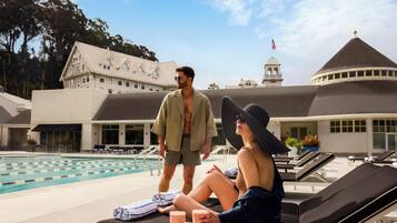 Zona junto a la piscina con sillones, una mesa con una fuente de fruta y un edificio con una torre de reloj al fondo.
