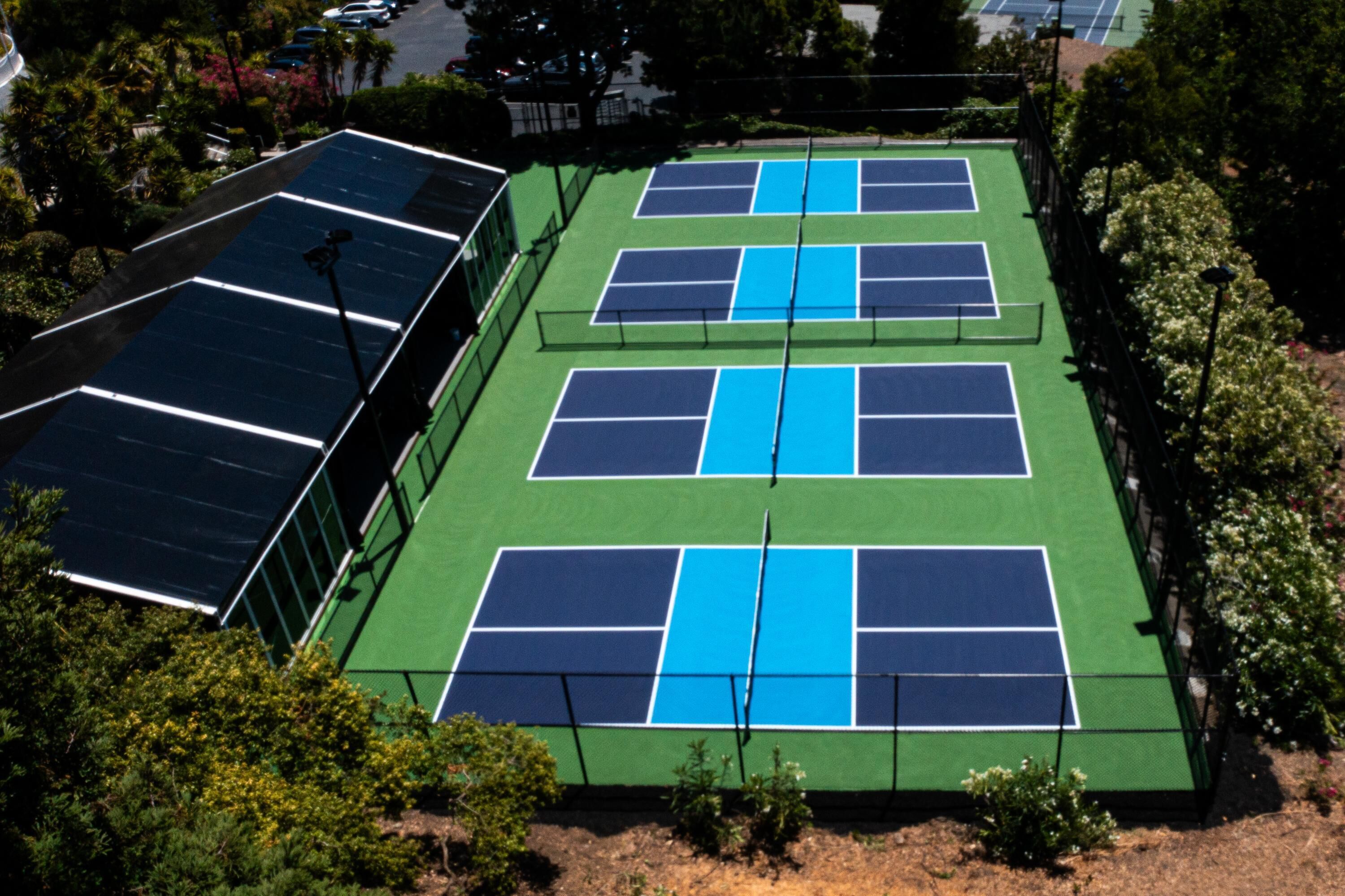 Pistas de tenis múltiples, rodeadas de vegetación y un edificio con paneles solares.