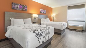 A hotel room with two beds, a nightstand, a lamp, and artwork on the wall.