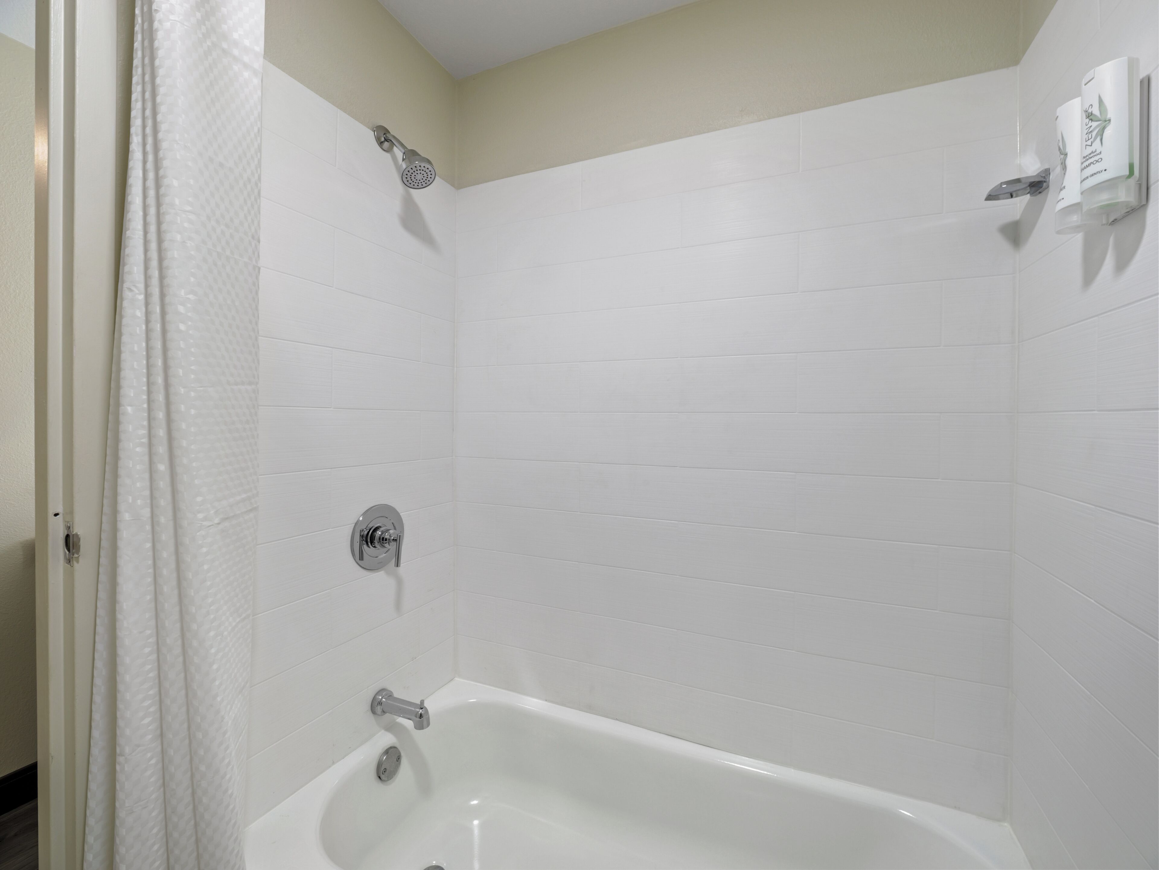 A bathroom with white tiled walls, a bathtub, a showerhead, and a toilet.