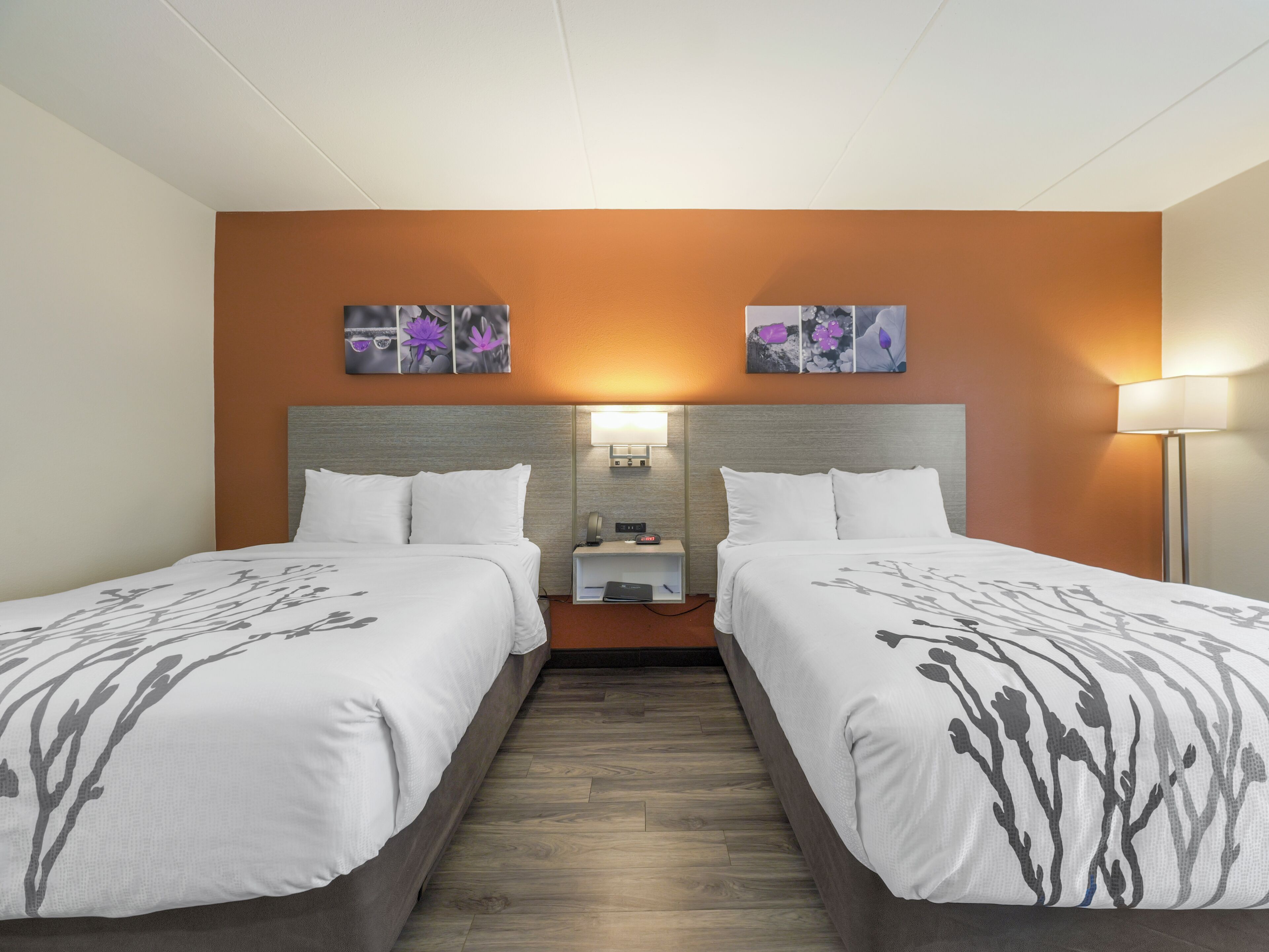 Una habitación de hotel con dos camas, una mesita de noche, una lámpara y una obra de arte en la pared.