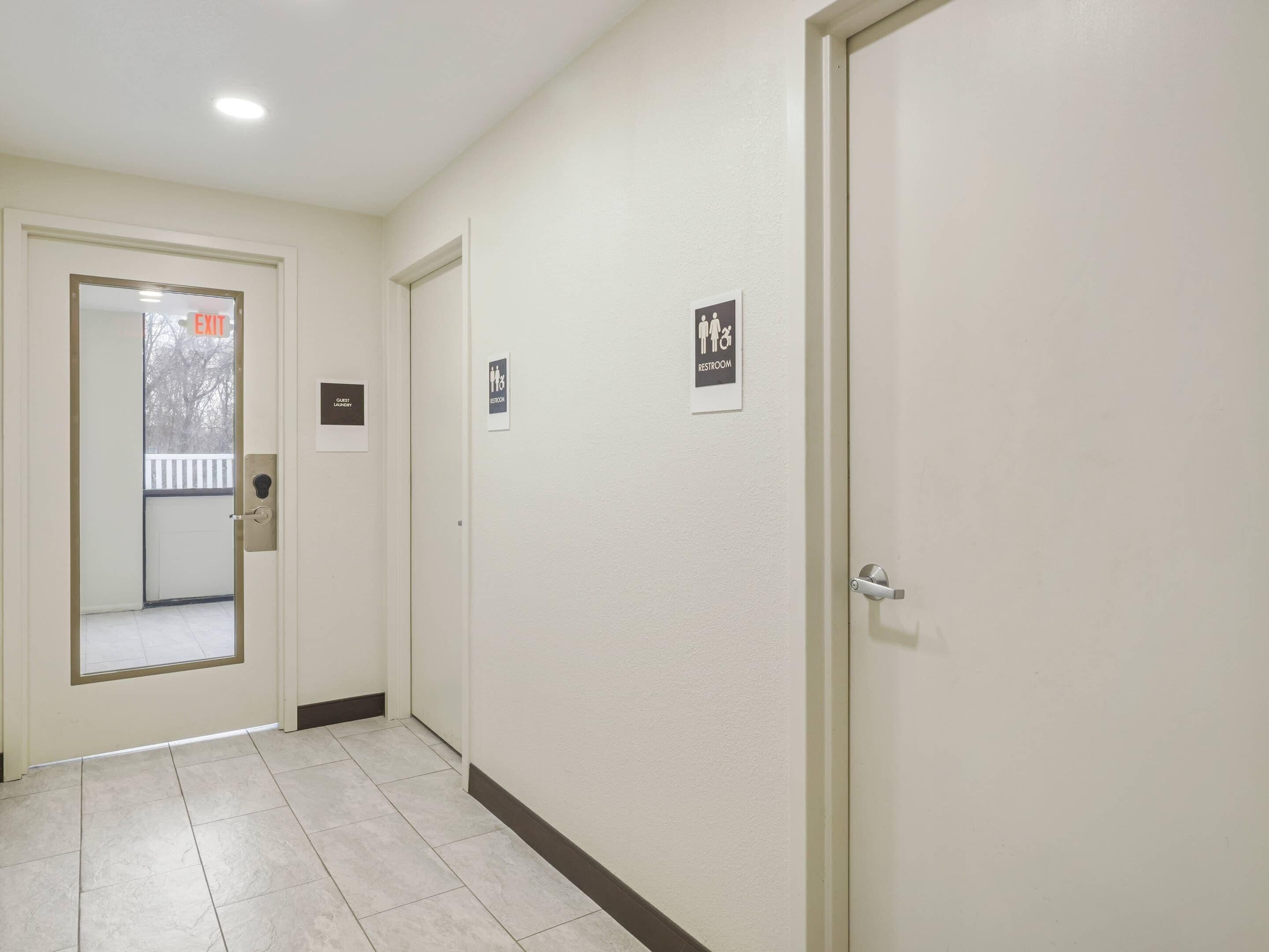 Een hal met een deur waarop 'EXIT' staat, een bordje 'RESTROOM' en een bordje 'GUEST LOBBY'.
