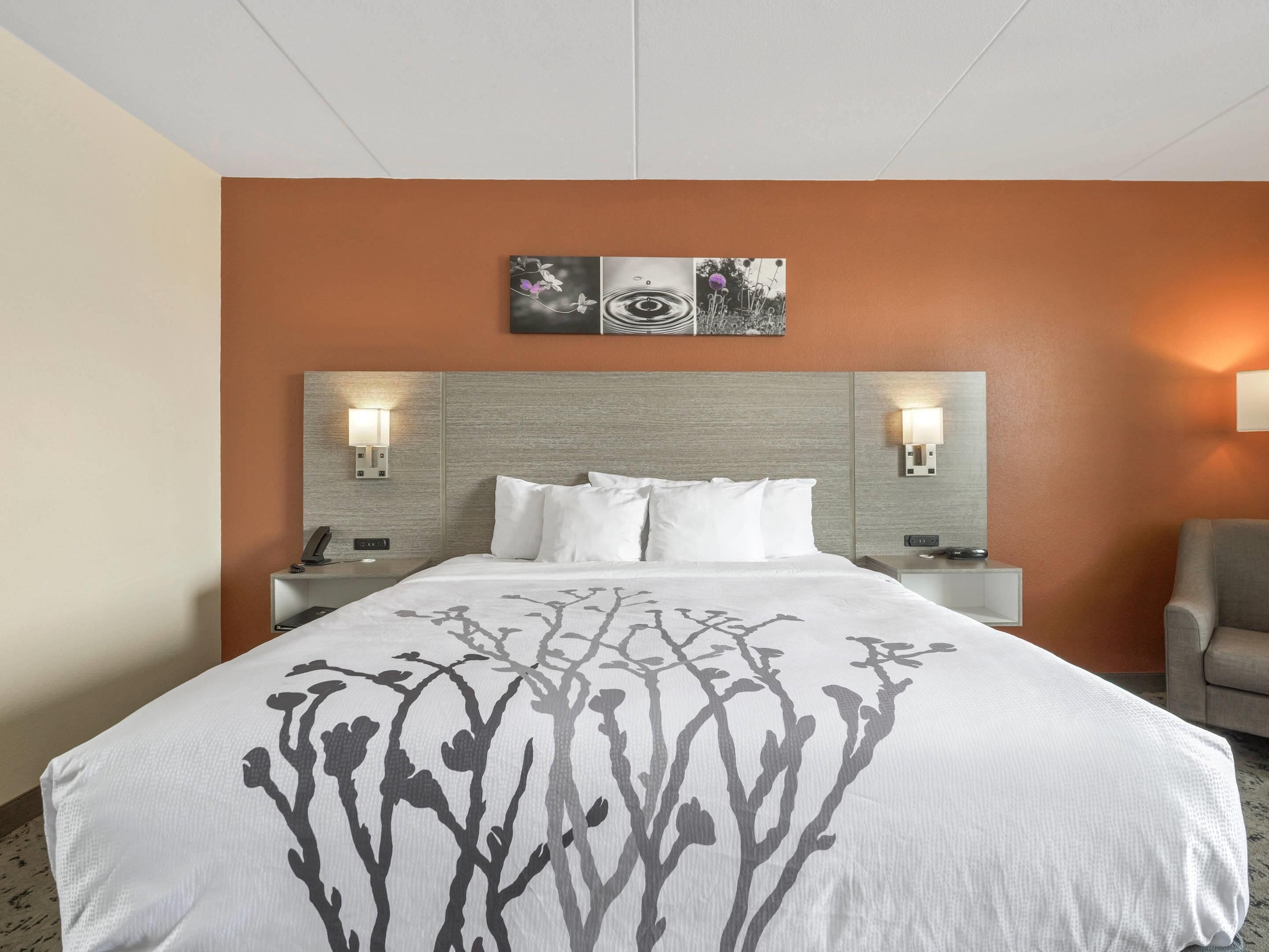 Ein Hotelzimmer mit einem großen Bett, zwei Nachttischen, einem Sessel und einem Wandbild über dem Bett.