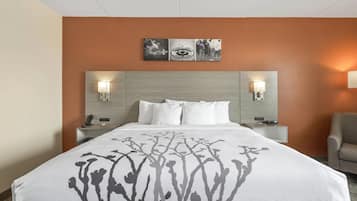 Ein Hotelzimmer mit einem großen Bett, zwei Nachttischen, einem Sessel und einem Wandbild über dem Bett.