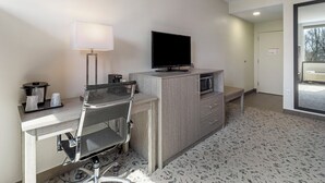 A hotel room with a desk, chair, television, lamp, and a microwave.