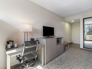 Quarto de hotel com escrivaninha, cadeira, televisão, luminária e micro-ondas.