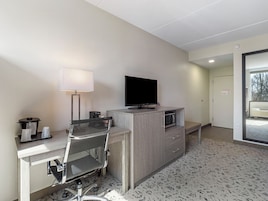 Habitación de hotel con escritorio, silla, televisión, lámpara y microondas.